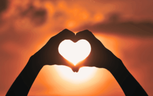 Hands forming heart shape at sunset symbolizing self-compassion and worth for trauma survivors releasing shame