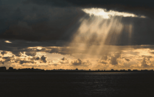 Dramatic sunlight breaking through dark storm clouds over water representing truth overcoming shame and hope in trauma recovery
